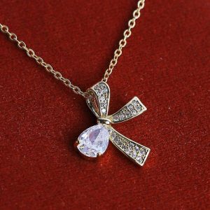 A Golden Necklace With A Captivating Bow Design, Featuring A Vibrant Oval-shaped Gemstone At Its Center
